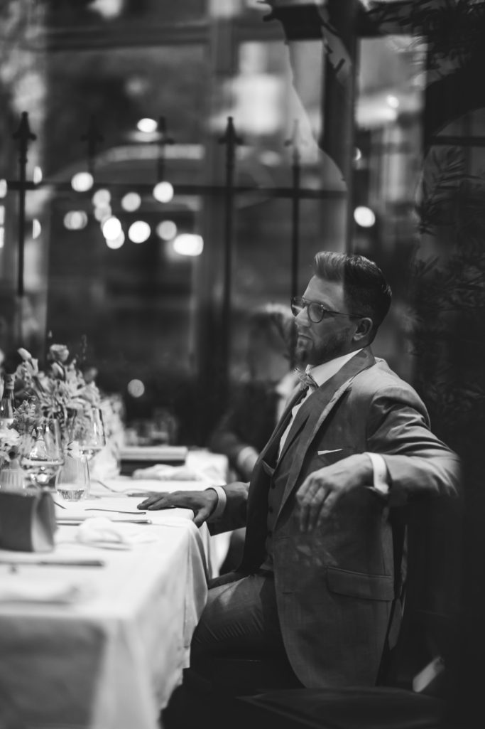 Ein Mann in Anzug sitzt an einem gedeckten Tisch in einem eleganten Restaurant.