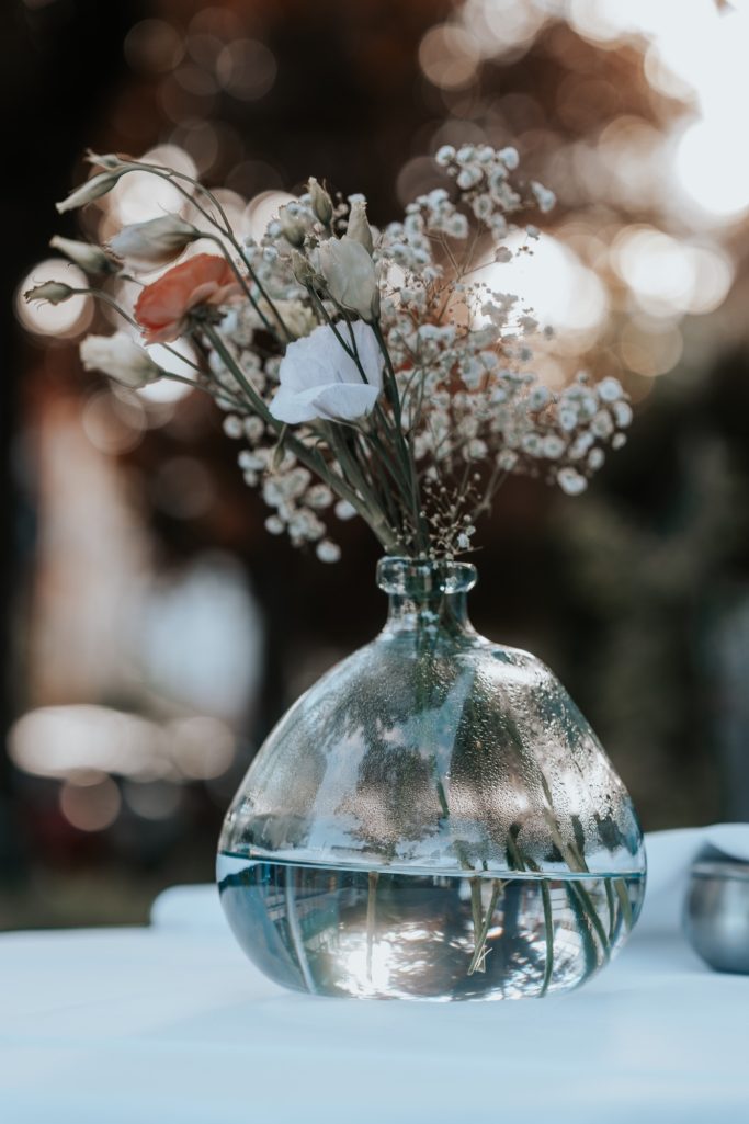 Glasvase mit Trockenblumen, auf einem Tisch im Freien.