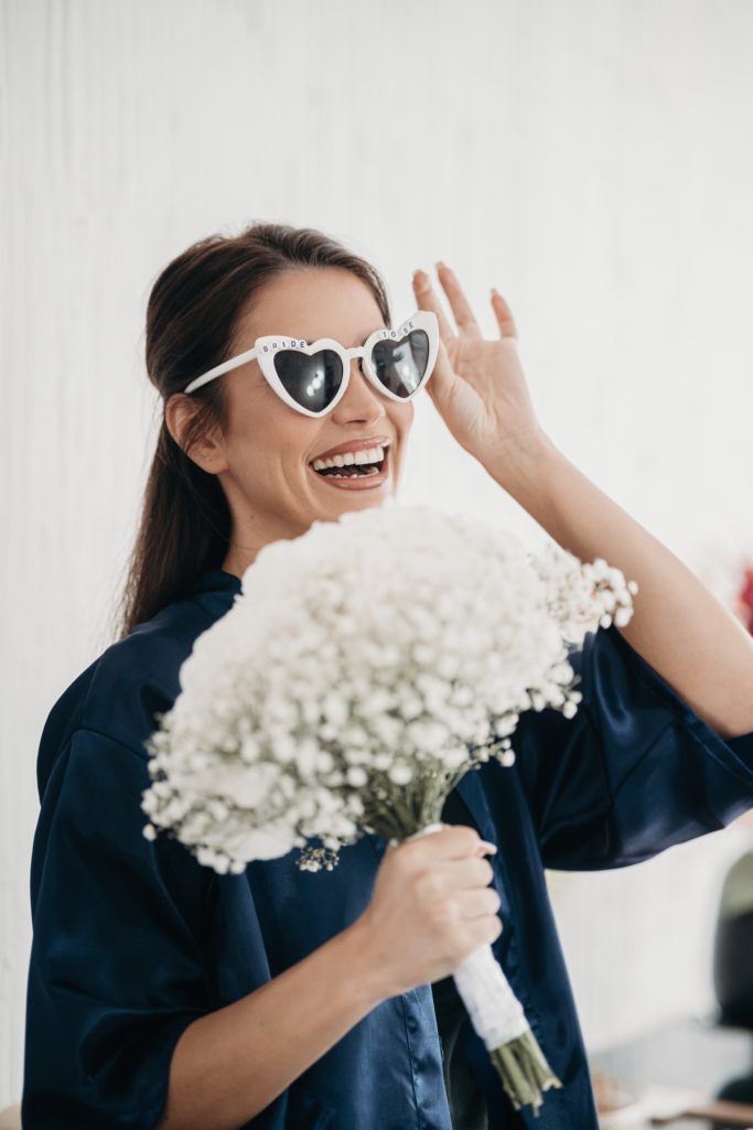 Lächelnde Frau mit Sonnenbrille hält einen Strauß aus Baby's-Breath-Blumen.