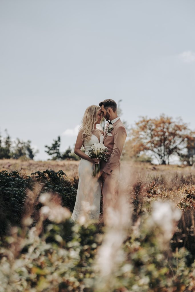 Ein Paar in Hochzeitskleidung umarmt sich vor einer ländlichen Kulisse.