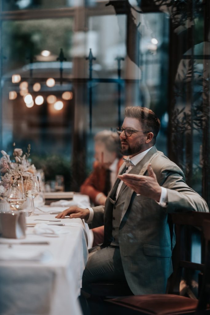 Ein elegant gekleideter Mann sitzt an einem festlich gedeckten Tisch in einem Restaurant.