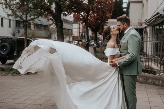 Braut und Bräutigam umarmen sich, die Braut trägt ein elegantes, fließendes Kleid.